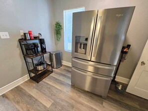 A kitchen with a stainless steel refrigerator, a coffee maker, a trash can, and a small plant. - The 11th Street Retreat (Temple)