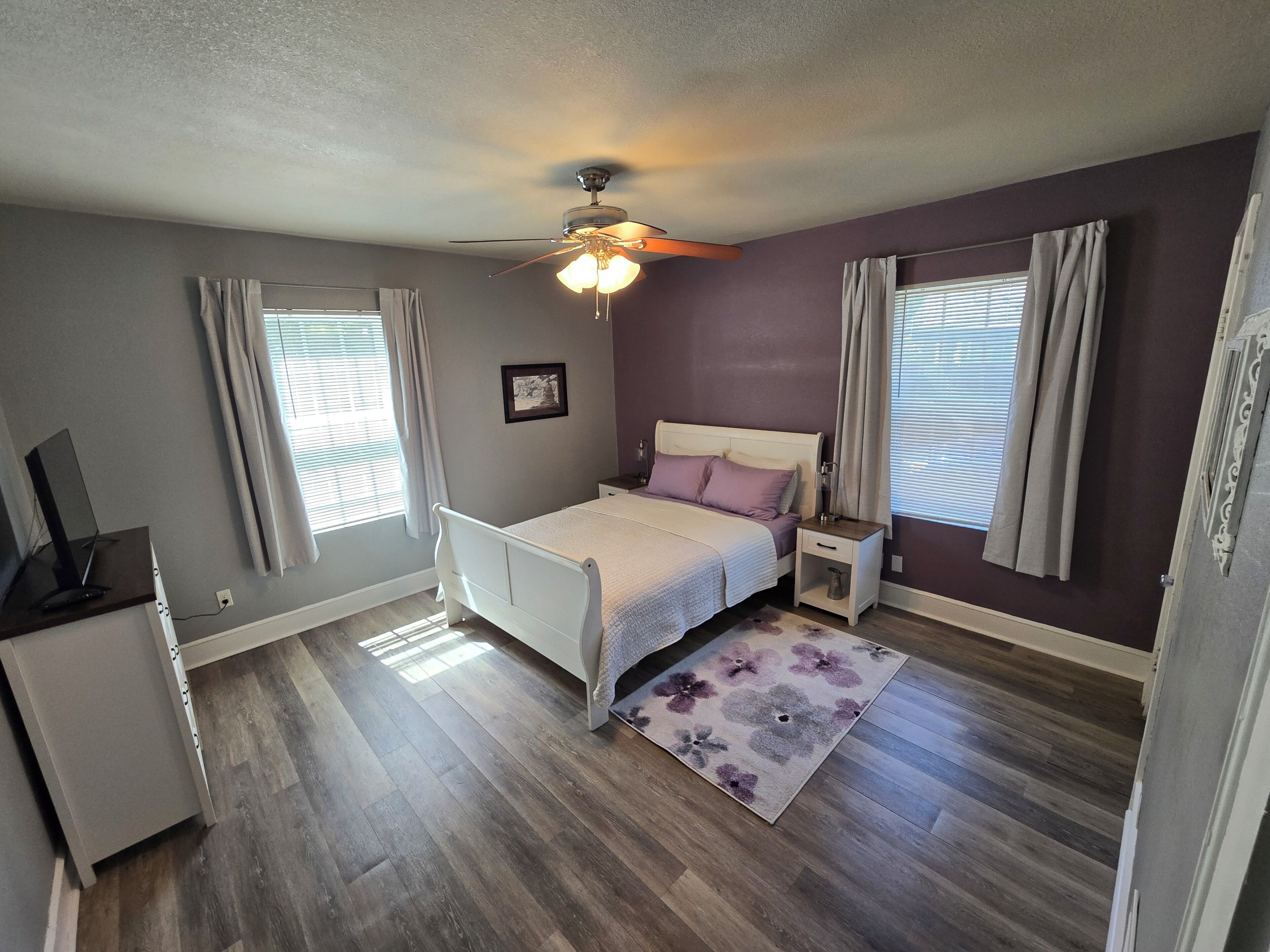 A bedroom with a bed, bedside tables, a ceiling fan, and a window with curtains.