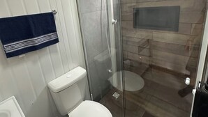 Et badeværelse med en glasafskærmet brusekabine, toilet og håndvask.