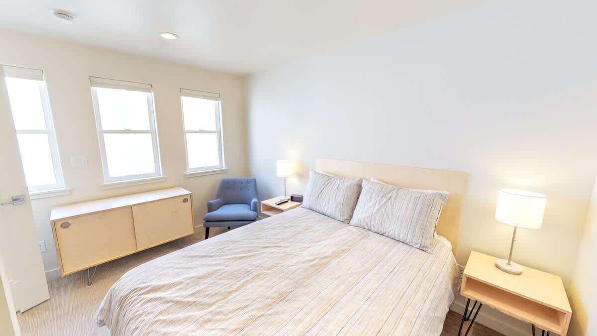 A bedroom with a bed, a chair, a bedside table, and a lamp.