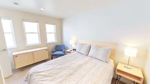 A bedroom with a bed, a chair, a bedside table, and a lamp.