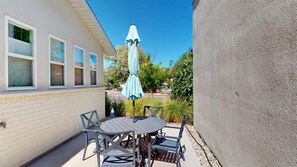 A patio with a round table and chairs, an umbrella, and a house with windows.