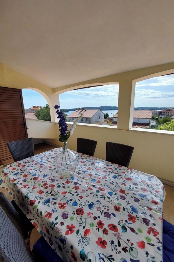 Un'area pranzo con tavolo apparecchiato per quattro persone, un vaso con fiori e vista su un lago e alcuni edifici.