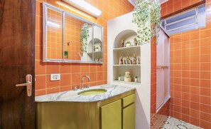 Ein Badezimmer mit orangefarbenen Fliesen, einem Waschbecken mit Marmorplatte und Regalen mit Dekoration.