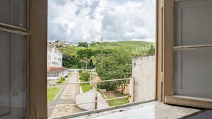 Blick durch ein offenes Fenster auf eine Straße, Gebäude und eine Hügelkulisse im Hintergrund.
