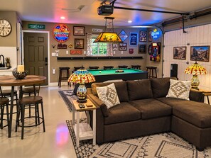 A room with a pool table, a brown sectional sofa, a bar area with a neon sign, and a projector mounted on the ceiling. - Prescott Spirits: A bar themed getaway, 7 minute drive to historic Whiskey Row (Prescott)