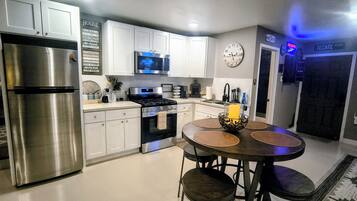 A modern kitchen with stainless steel appliances, white cabinetry, a round dining table with stools, and a clock on the wall.