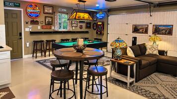Un espace bar avec une table de billard, des tabourets et un panneau lumineux au néon.