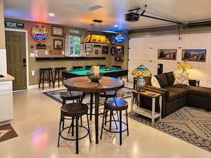 A bar area with a pool table, stools, and a neon sign.