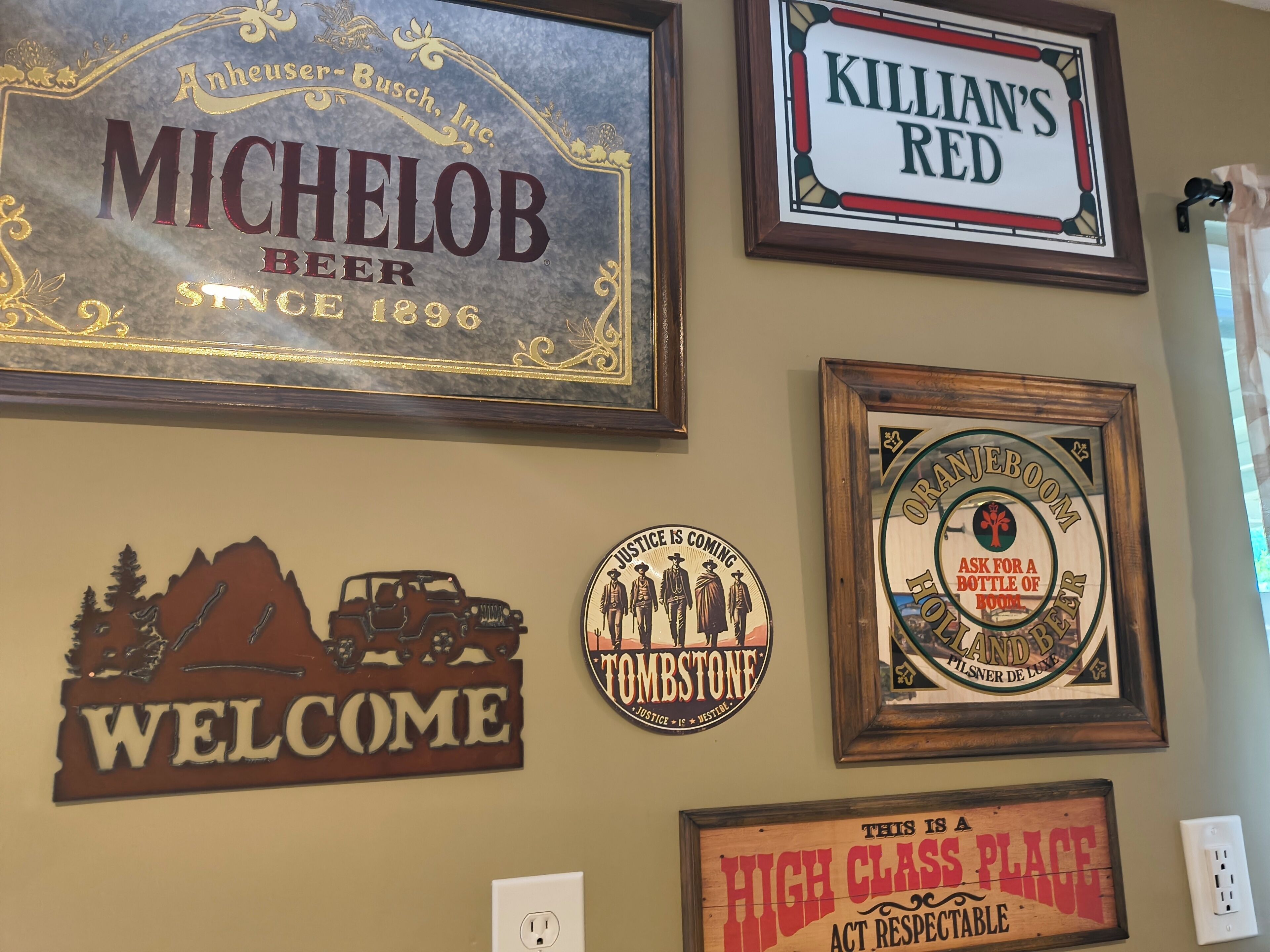 A wall with various framed signs including 'MICHELOB BEER,' 'WELCOME,' 'TOMBSTONE,' 'KILLIAN'S RED,' and 'HIGH CLASS PLACE.'