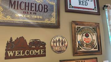 A wall with various framed signs including 'MICHELOB BEER,' 'WELCOME,' 'TOMBSTONE,' 'KILLIAN'S RED,' and 'HIGH CLASS PLACE.'