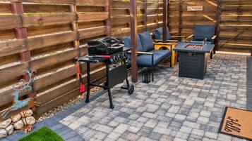 Un patio al aire libre con una parrilla, zona de estar y valla de madera.