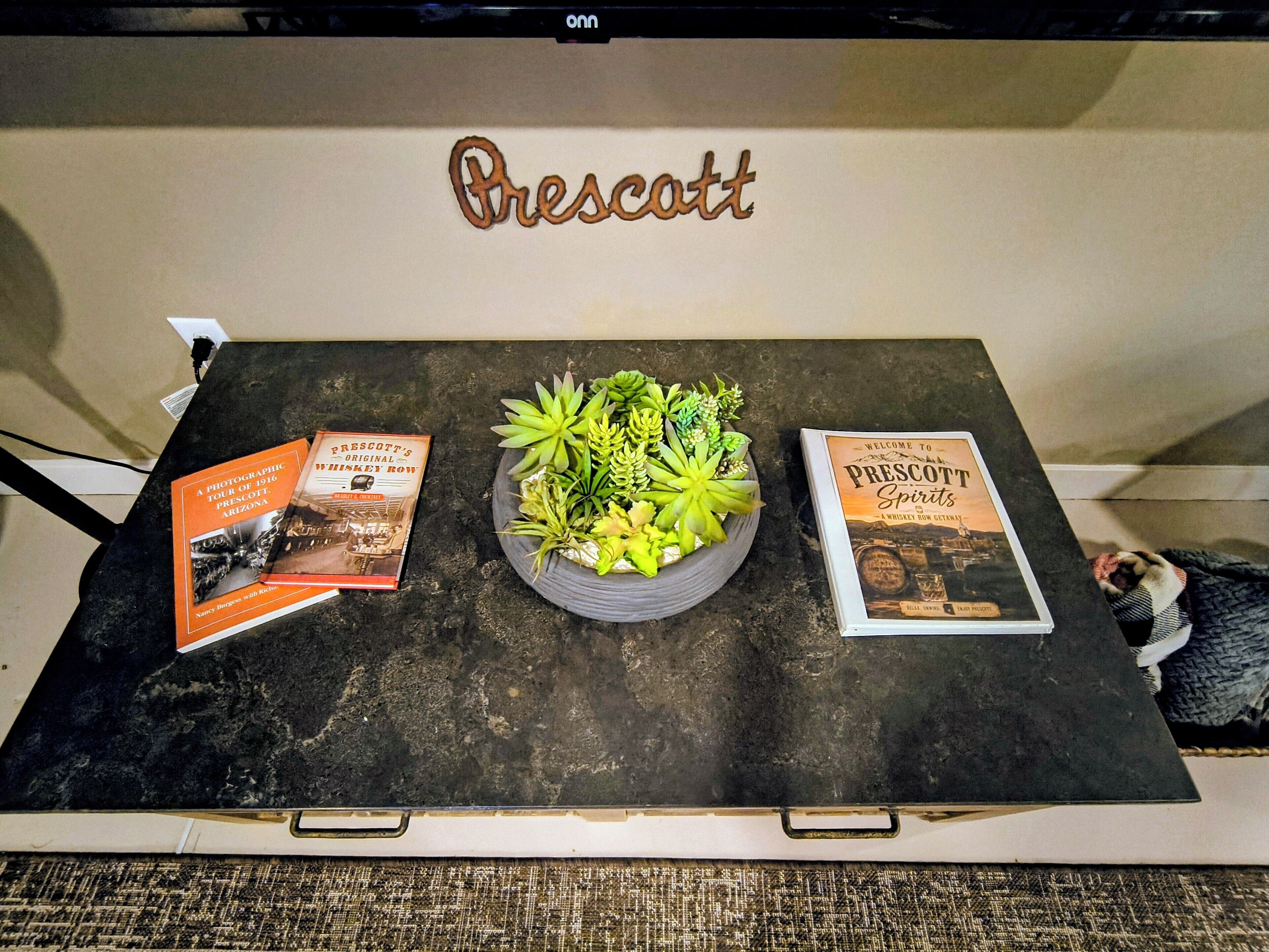 Una mesa con dos libros titulados 'Prescott Spirits' y 'Prescott's Original Whiskey Row', junto con una planta en maceta.