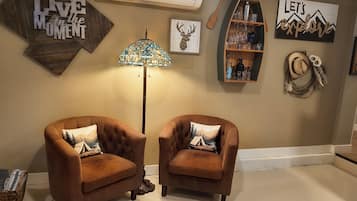 A room with two brown armchairs, a floor lamp, and wall decorations including 'LIVE in the MOMENT' and 'LET'S explore' signs.