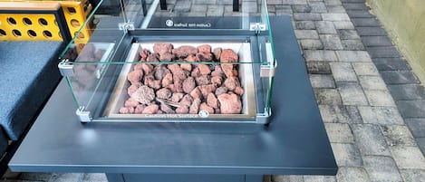 A glass enclosure with a warning label, containing what appears to be hot rocks, on a black table with a metal frame.