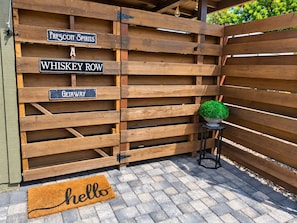 Una puerta de madera con letreros que indican 'Prescott Spirits', 'Whiskey Row' y 'Getaway'. También se ve una planta en maceta y un felpudo con la palabra 'hello'.