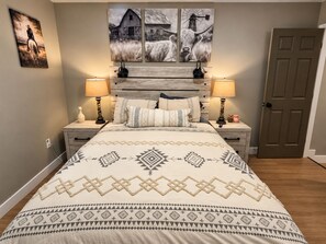 Un dormitorio con cama, dos mesitas de noche, una puerta y decoración en la pared.