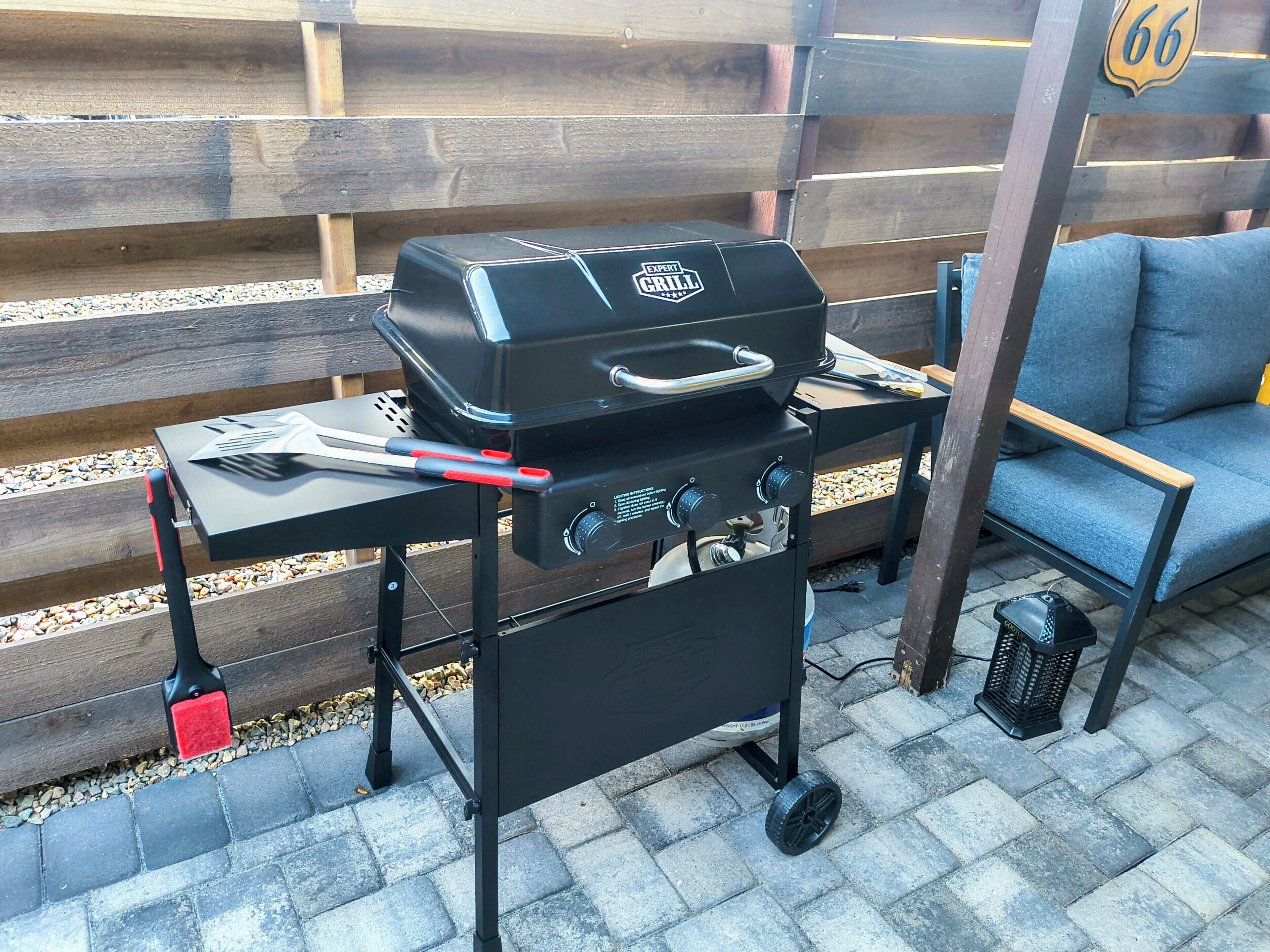 Una parrilla portátil con controles y asa, una silla plegable y un cesto de basura pequeño.