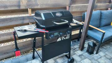 Una parrilla portátil con controles y asa, una silla plegable y un cesto de basura pequeño.