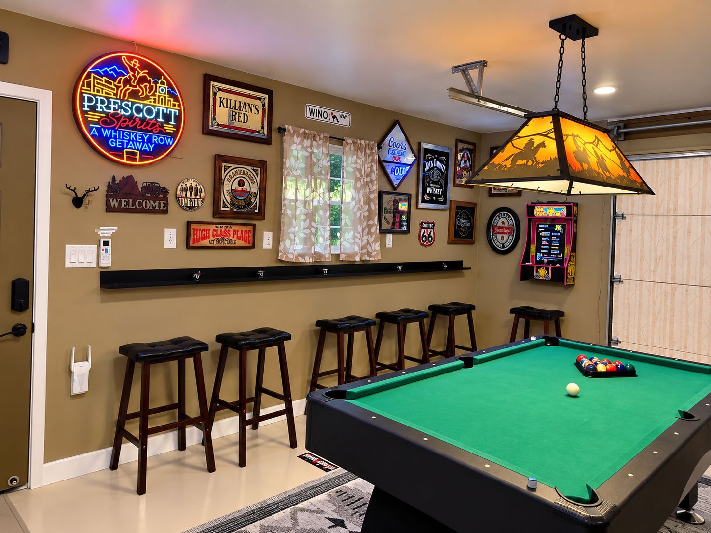 A pool table with a neon sign, bar stools, and various framed memorabilia on the wall.