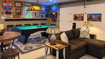 Una habitación con mesa de billar, sofá y zona de bar con letrero de neón.
