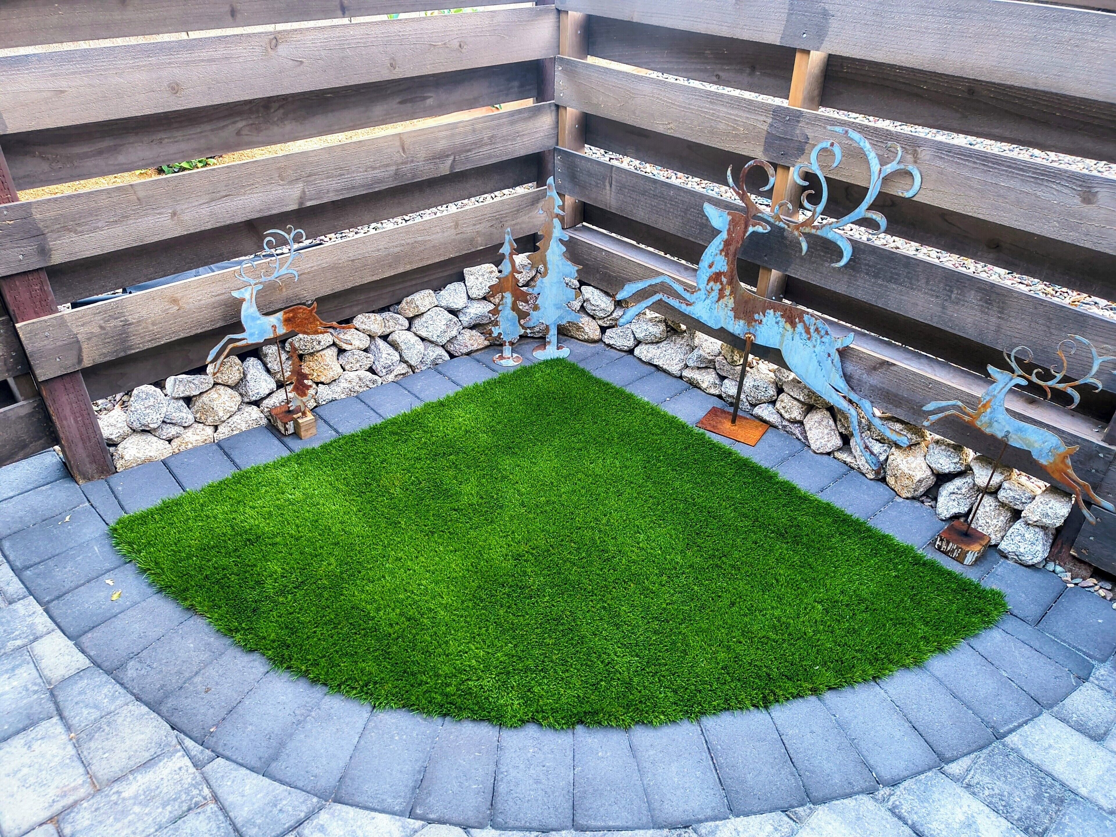 Un espace jardin agrémenté d’une pelouse verdoyante au centre, bordée d’une murette en pierre et décoré de sculptures de cerfs en métal.
