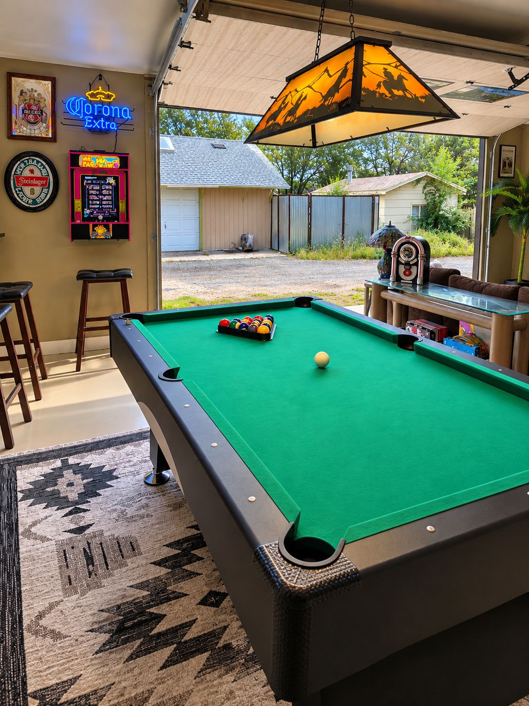 Een pooltafel met een groene viltkleed, een neonbord en uitzicht op een achtertuin.