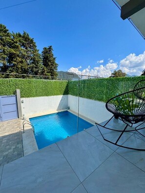 A swimming pool with a tiled deck, surrounded by a green hedge, and a chair. - Dianas Home Valle de Bravo (santa maria pipioltepec)