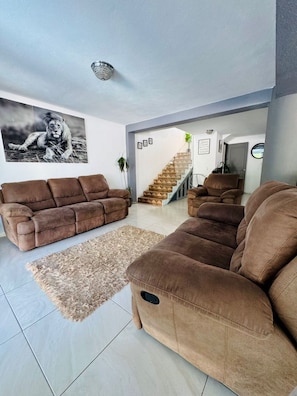 Ein Wohnzimmer mit zwei braunen Sofas, einem Hochflor Teppich und einer Treppe, die in einen anderen Raum führt.