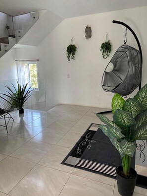 A spacious room with a high ceiling, a hanging chair, potted plants, and a staircase. - Dianas Home Valle de Bravo (santa maria pipioltepec)