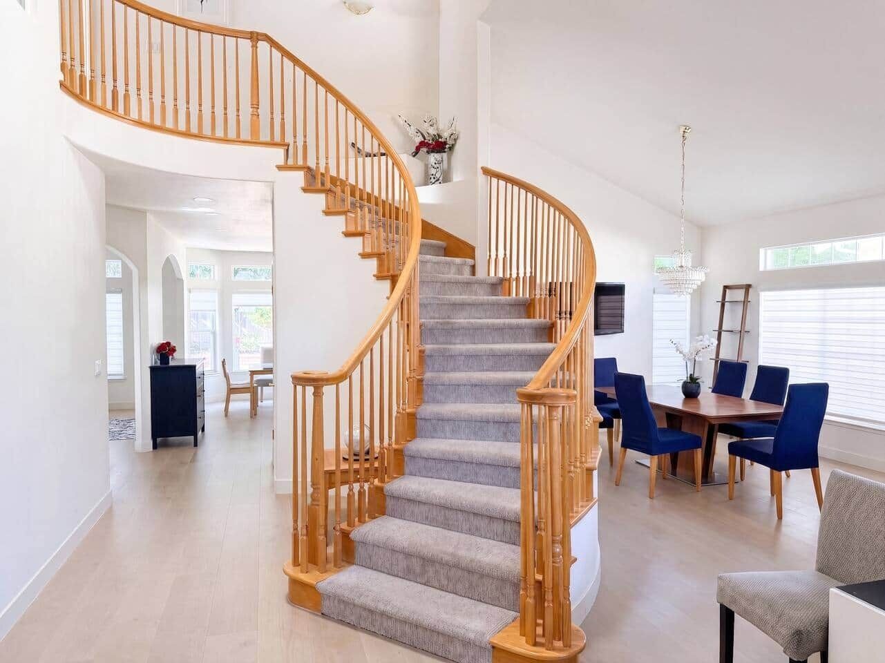 Un vaste espace de vie agrémenté d’un escalier en bois, d’une table à manger avec des chaises et d’un lustre.