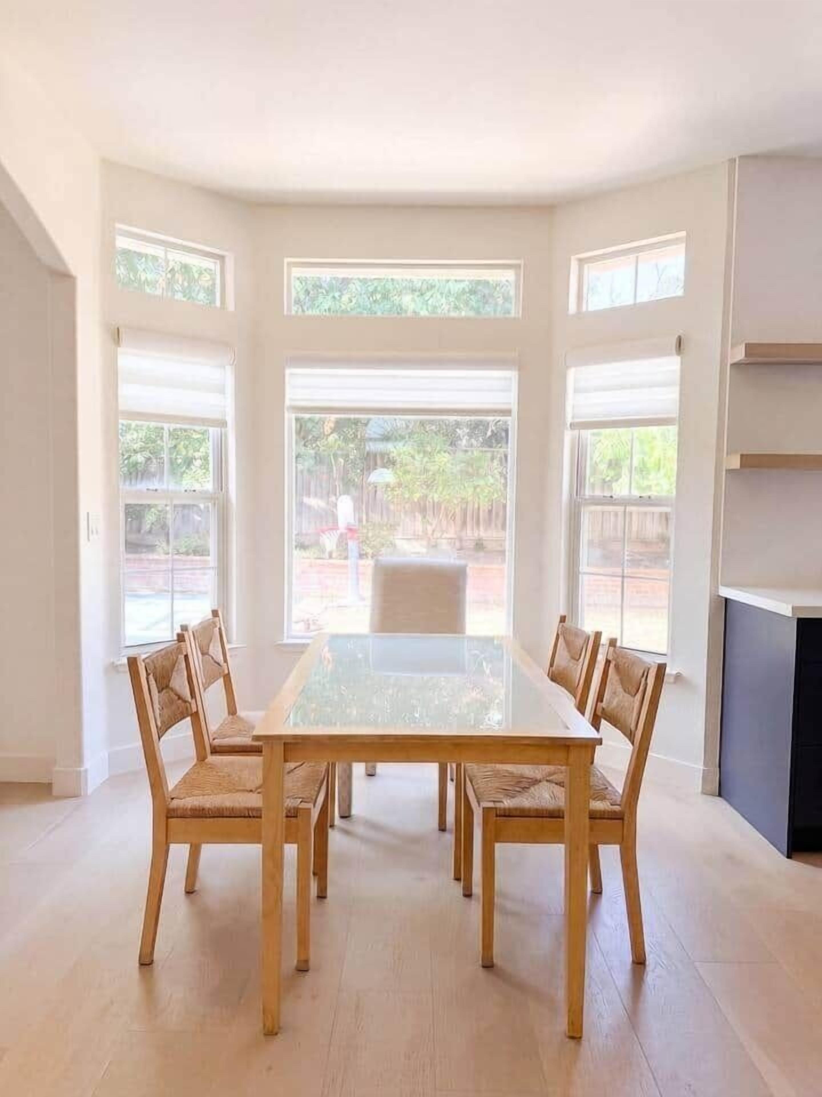 Un espace repas comprenant une table rectangulaire et six chaises, de grandes fenêtres et une cheminée.