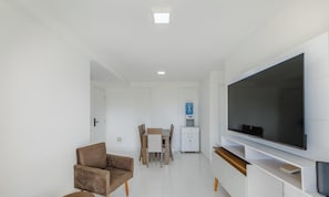 Uma sala de estar moderna com televisão de tela plana, uma poltrona marrom, uma mesa de jantar com cadeiras e um purificador de água.