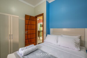 A neatly made bed with white linens and pillows, a wooden wardrobe, and a blue accent wall. - House With Barbecue and 2 Bedrooms Rek0001 (Penha)