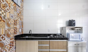 Cuina amb rajoles decoratives, taulell negre, fogó, microones i armaris de fusta.