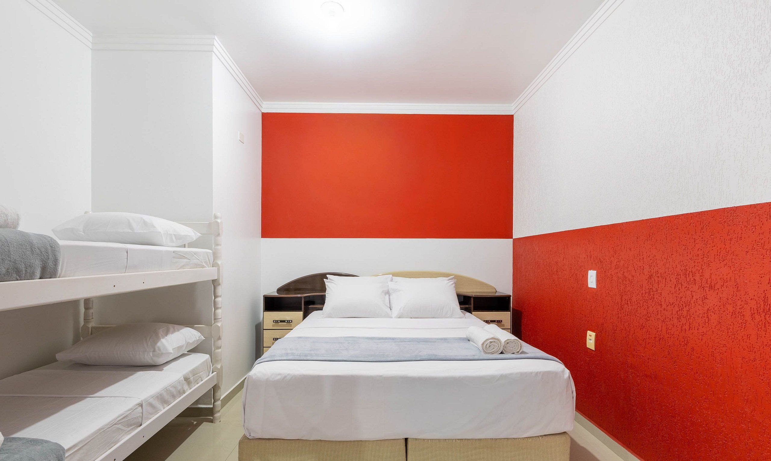 Habitación de hotel con literas, una cama individual y una pared de acento roja.