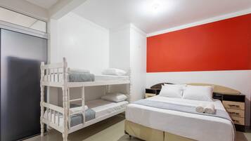 Habitación de hotel con literas, una cama individual, una pared de acento roja, una mesita de noche y un armario.