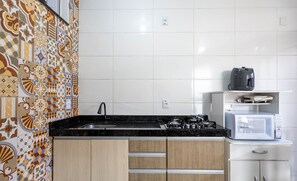 Uma cozinha com bancada preta, pia, fogão e micro-ondas.