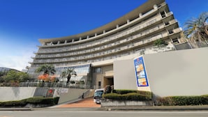 A multi-story hotel with a curved facade, balconies on each floor, and a parking area in front. - KKR Hotel Atami (Atami)