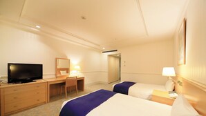A hotel room with a desk, a television, two beds, a mirror, and a door leading to a bathroom. - KKR Hotel Atami (Atami)