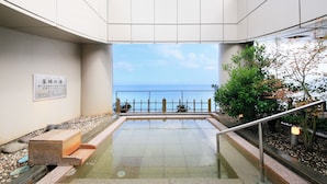 A pool area with a view of the sea, a wooden deck, and a stone bench. - KKR Hotel Atami (Atami)