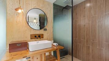 Un baño moderno con tocador de madera, espejo redondo, lavabo blanco y cabina de ducha con mampara de vidrio.