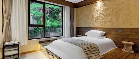 A bedroom with a large window, a bed with white linens, a small bedside table, and a wall-mounted shelf.