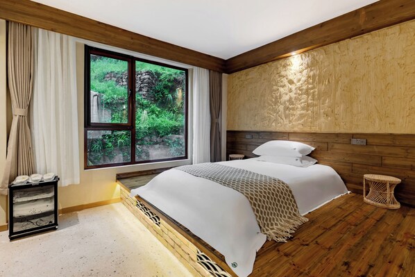 A bedroom with a large window, a bed with white linens, a small bedside table, and a wall-mounted shelf.