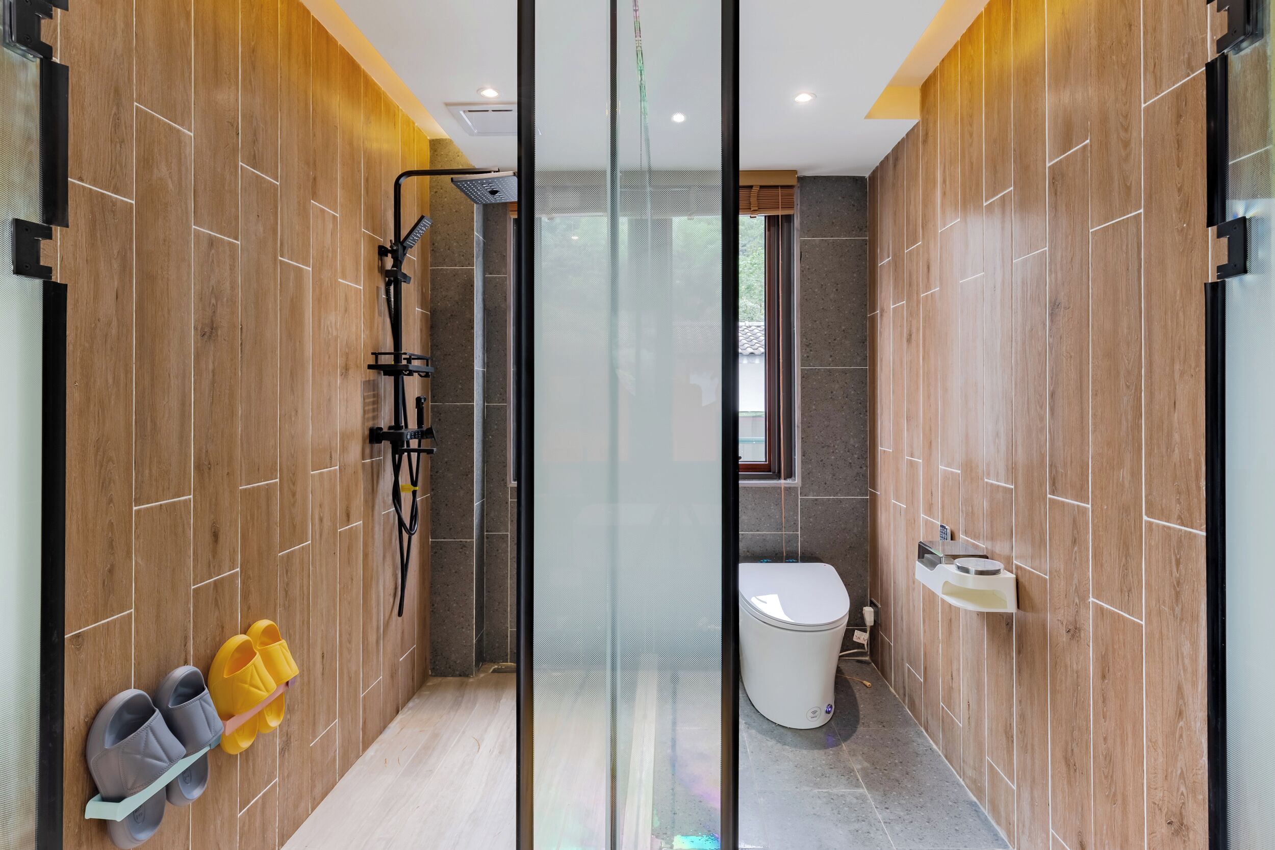 Un baño moderno con paneles de madera, cabina de ducha de vidrio y un inodoro con lavamanos.