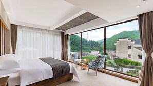A modern hotel room with a large bed, a view of a mountainous landscape, and a balcony with seating. - Mount Huangshan Wen'an B&B (Huangshan)