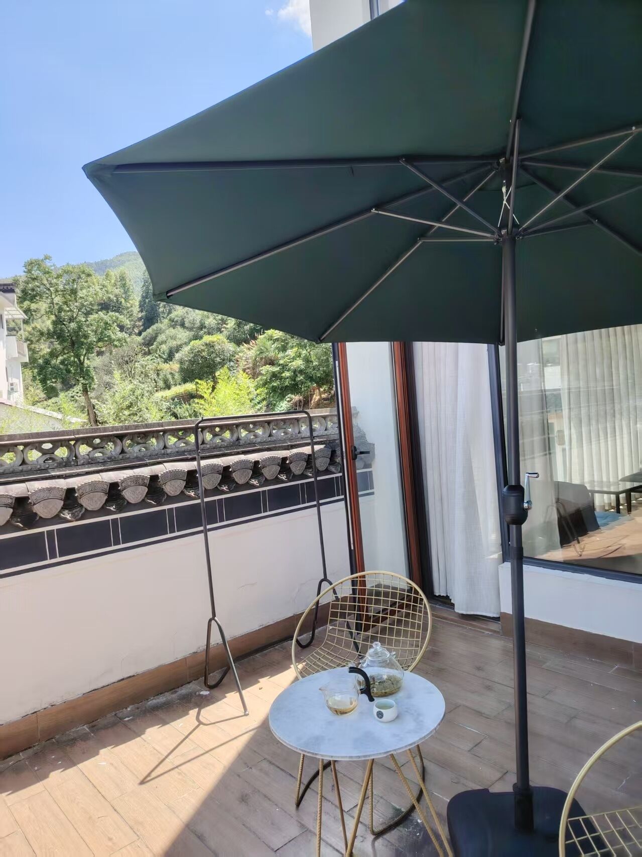Un balcón con una mesa, sillas y un amplio paraguas.