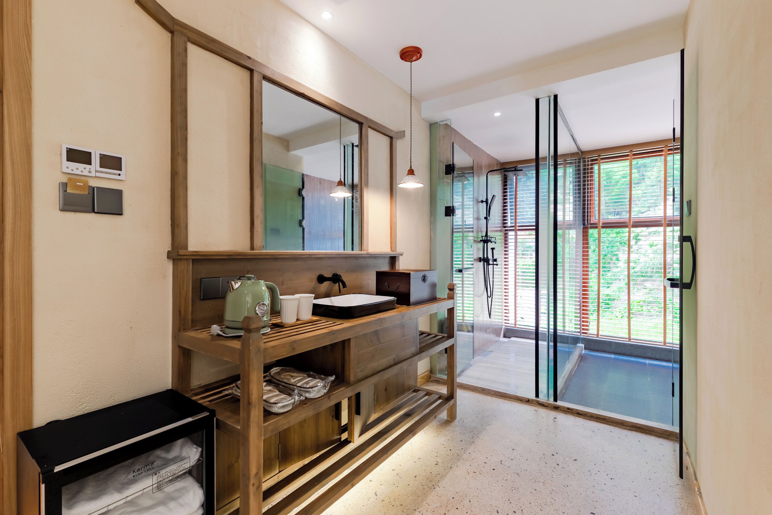 A modern bathroom with a wooden vanity, a large mirror, a glass shower enclosure, and a view of greenery outside.