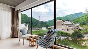 A room with large windows, a sofa, a small table, and a chair with a patterned cushion. - Mount Huangshan Wen'an B&B (Huangshan)