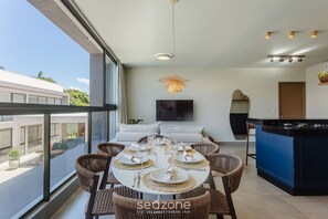 A modern dining area with a round table set for six, surrounded by wicker chairs, a hanging light fixture, and a kitchen island with a blue countertop. - Apt 350m From the Beach in Condo w/ Pool Bbc0102 (Maraú)